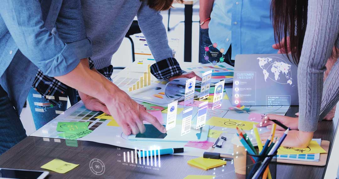 Brand Marketing Cover Image - People gathered around a table with papers, and digitalized graphics coming up from the table.